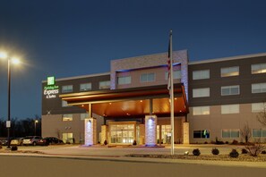 A Holiday Inn Express & Suites building with a modern design, featuring a prominent entrance with a covered walkway and illuminated signage.