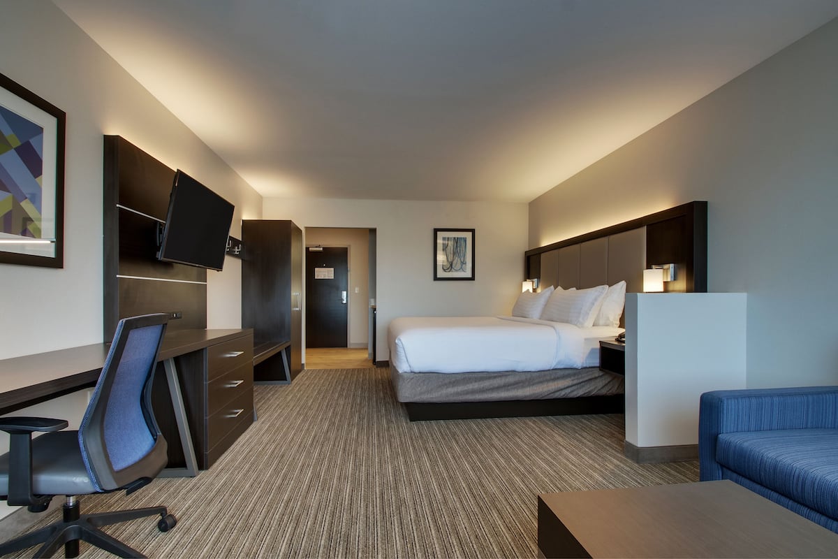 A hotel room with a bed, desk, chair, and a television on the wall.