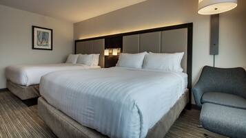 A hotel room with two beds, a chair, and a lamp.