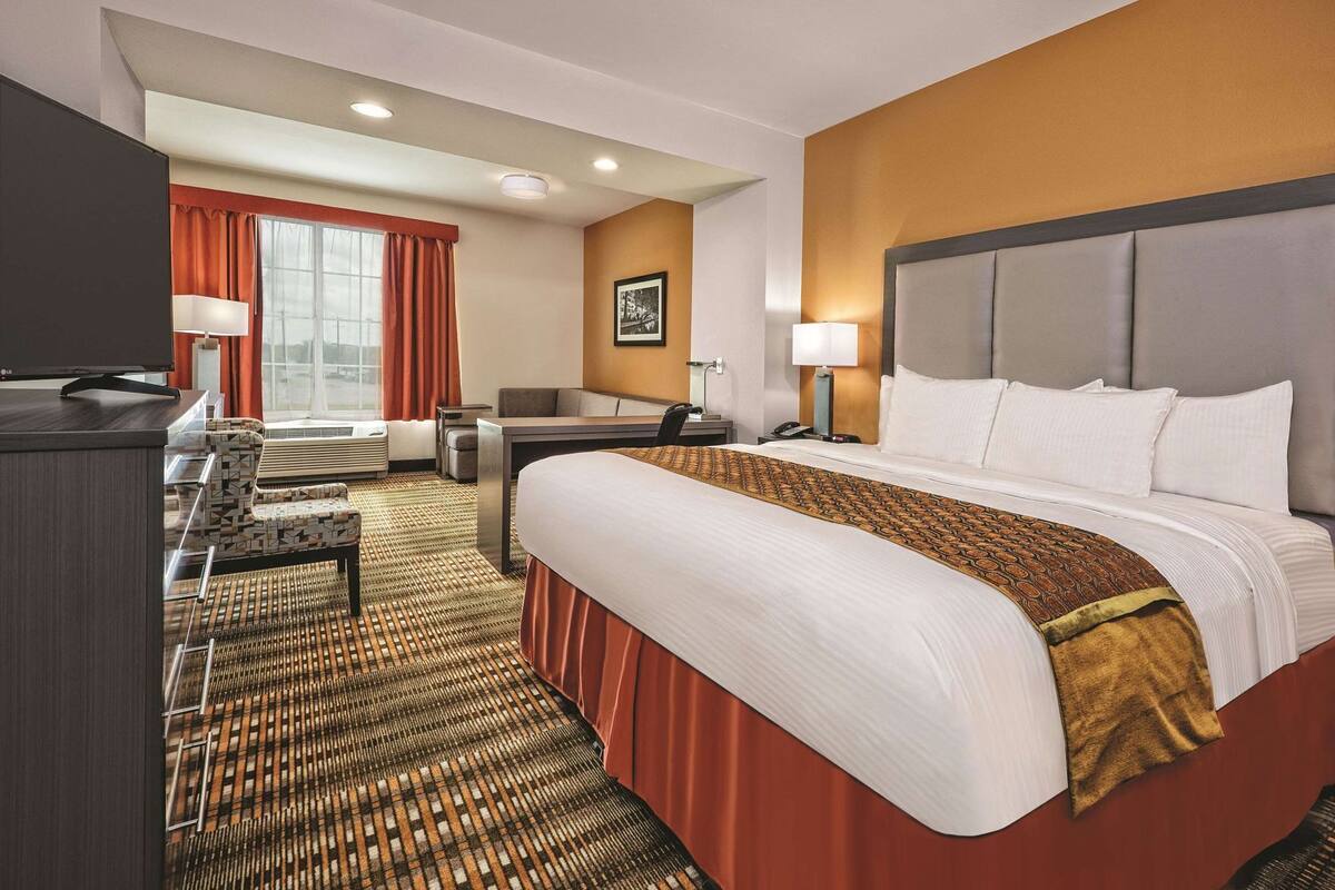 A hotel room with a bed, desk, chair, and a TV.