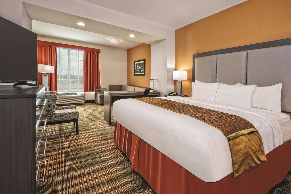 A hotel room with a large bed, a desk, a chair, a television, and a window with curtains.