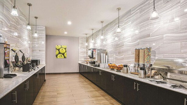 A modern kitchen with a long counter, overhead lighting, and a central island with appliances. - La Quinta by Wyndham San Antonio by Frost Bank Center (San Antonio)
