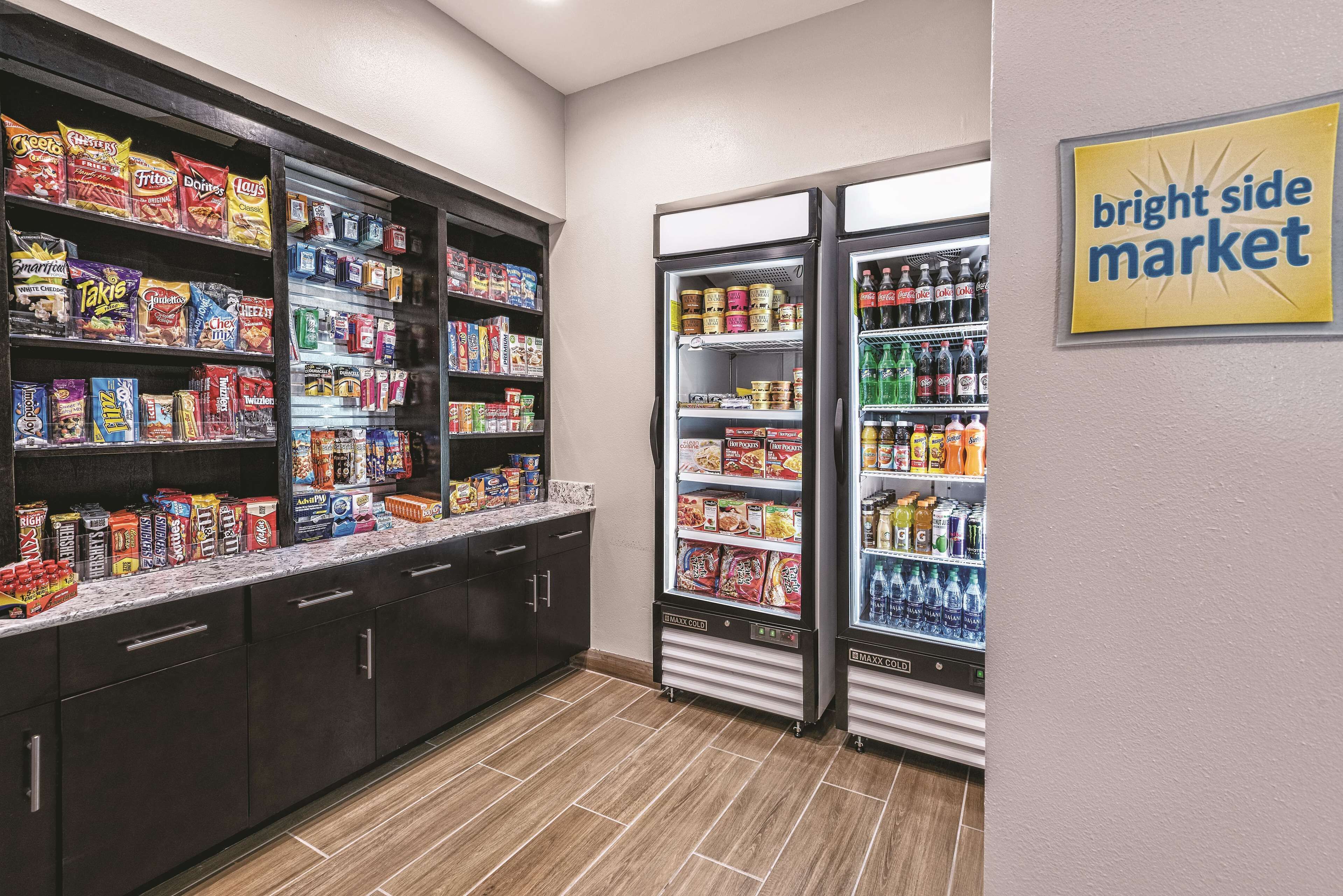 A self-service snack and beverage area with shelves stocked with various snacks and drinks, and two refrigerators.