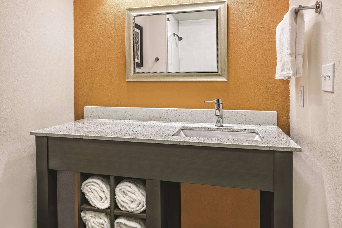 A bathroom with a granite countertop sink, a mirror, and a towel rack.