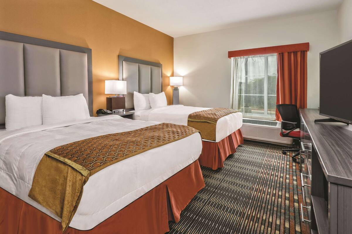 A hotel room with two beds, a desk, a chair, and a television.