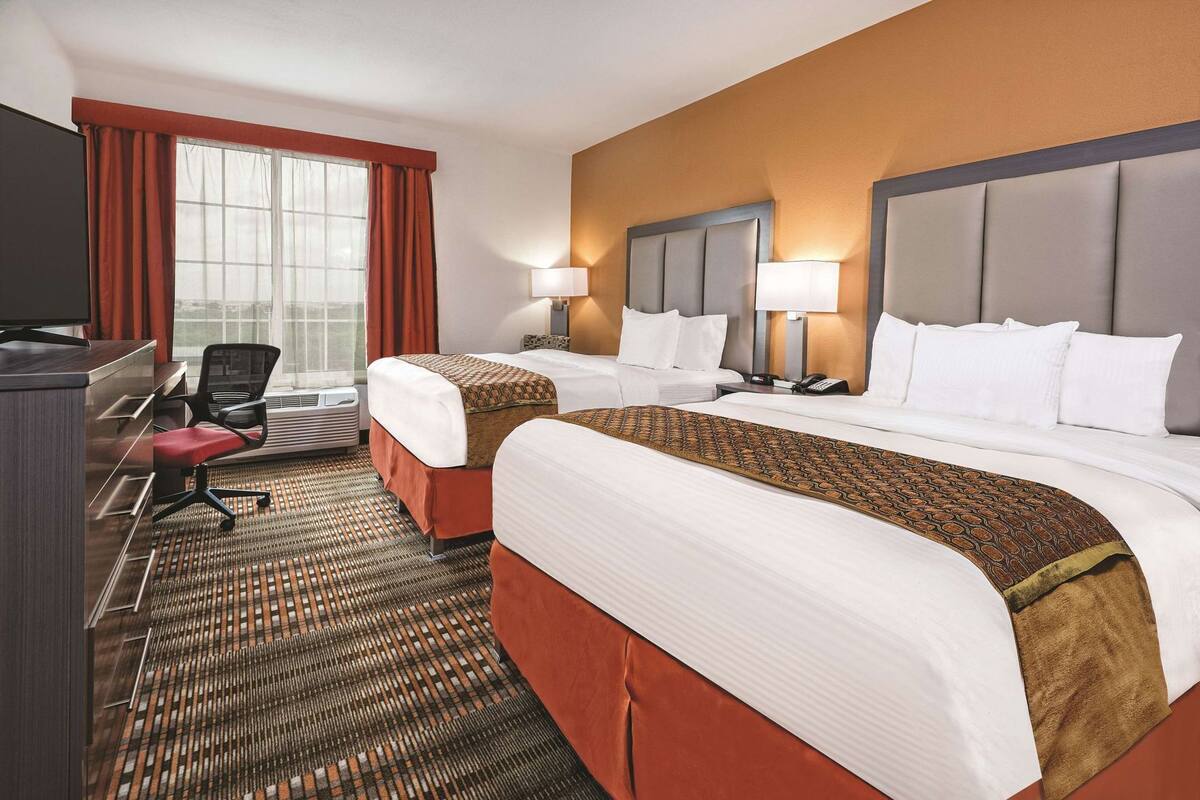 A hotel room with two beds, a desk, a chair, a TV, and a window with curtains.