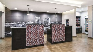 A modern reception area with a cityscape mural, two reception desks, and a vending machine. - La Quinta by Wyndham San Antonio by Frost Bank Center (San Antonio)