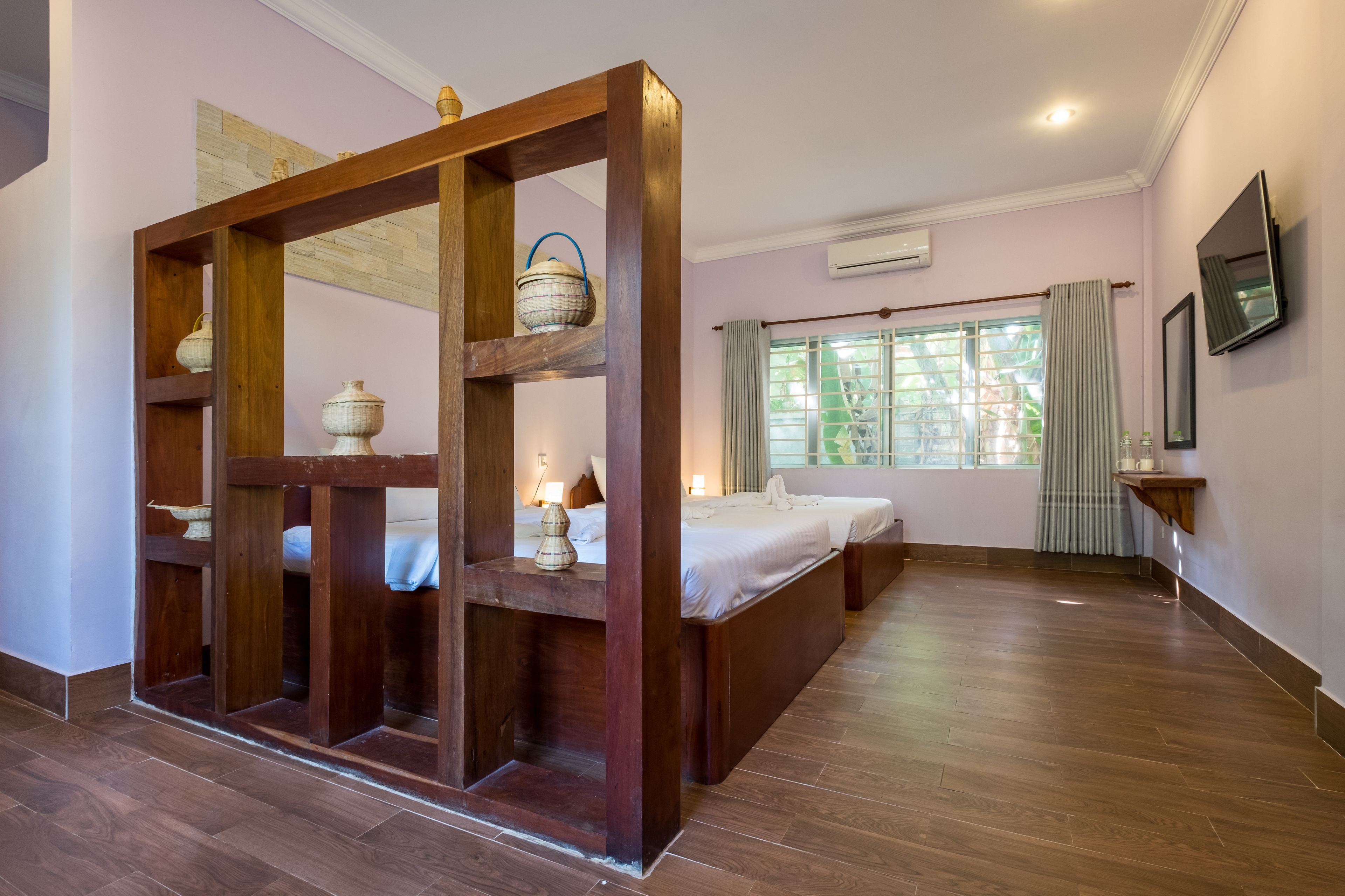 Quarto com estrutura de cama de madeira, duas mesas de cabeceira com luminárias, janela com cortinas e televisão fixada na parede.