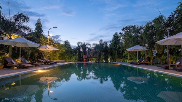 Una piscina con sillas de descanso y sombrillas, rodeada de abundante vegetación.