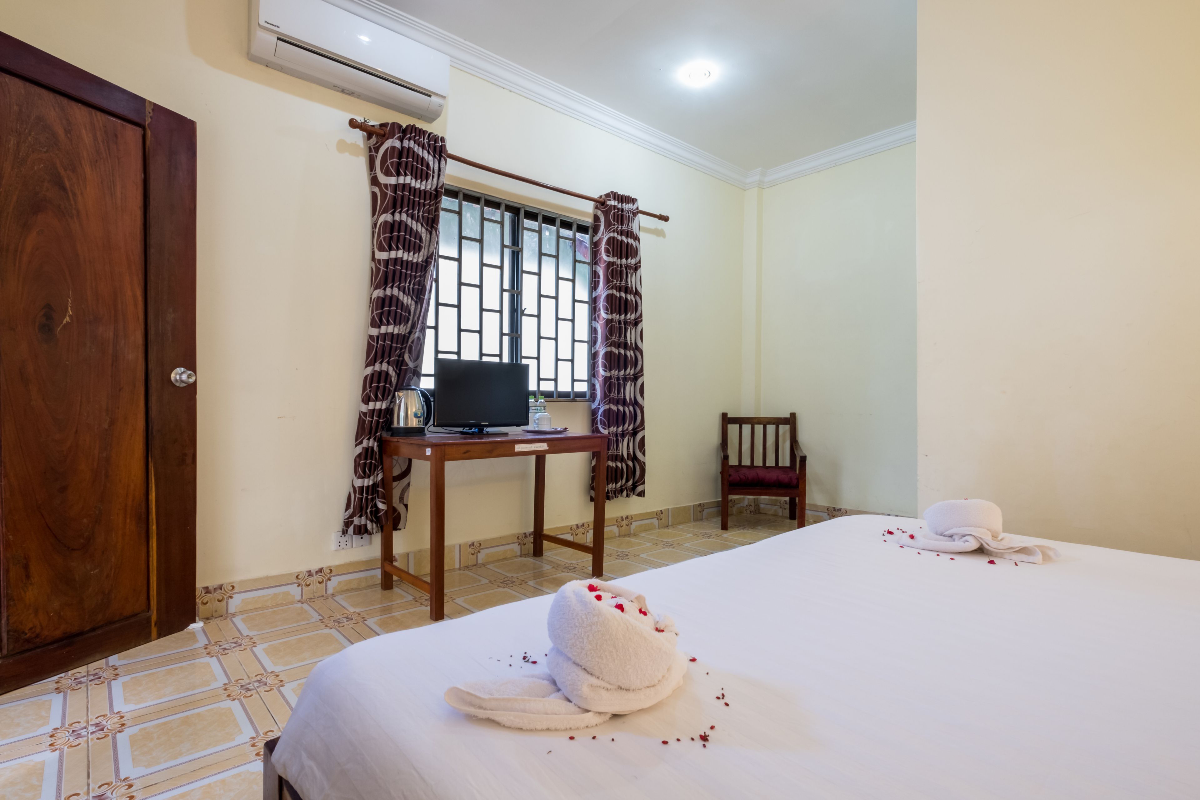 A hotel room with a bed, a desk with a laptop, a chair, and a window with curtains.