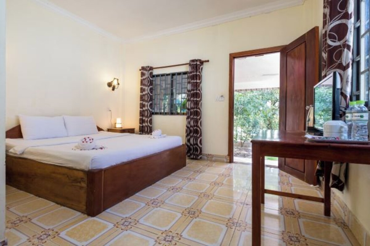 A bedroom with a bed, a nightstand, a table, and a window with curtains.