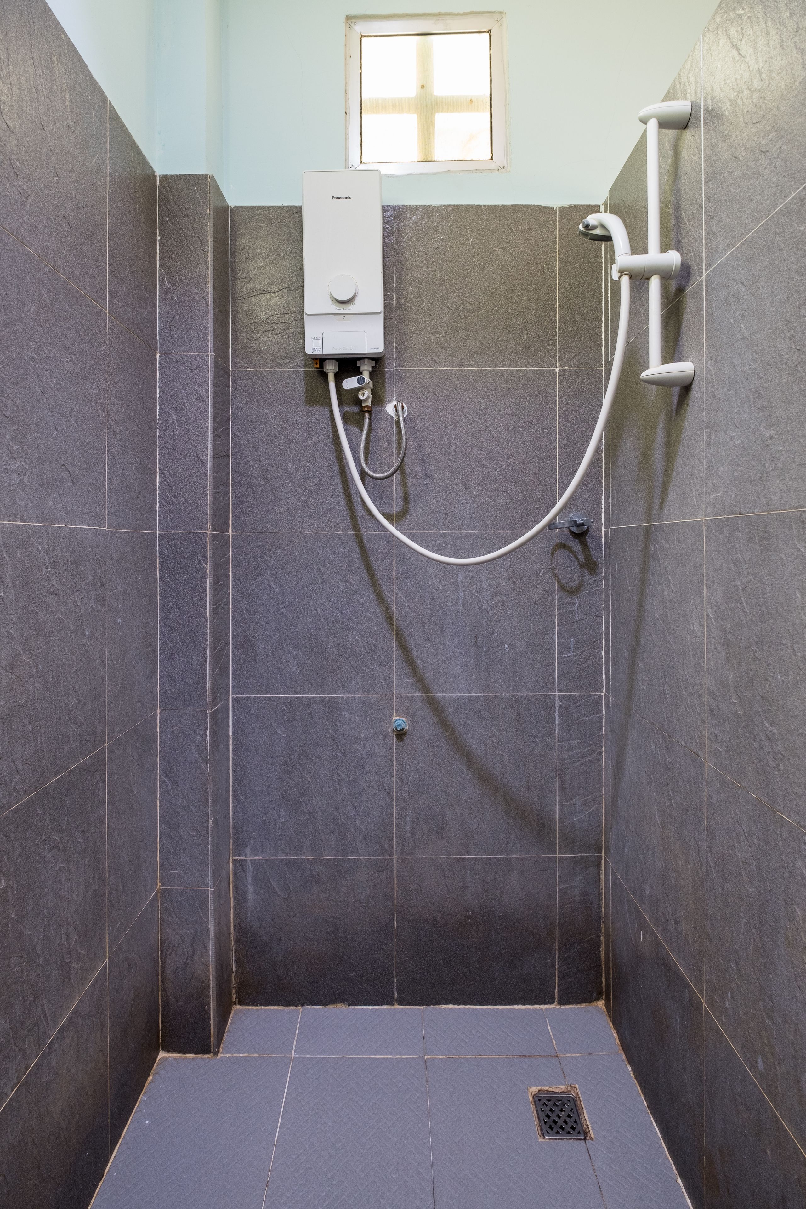 A shower area with dark tiles, a handheld showerhead, and a wall-mounted faucet.