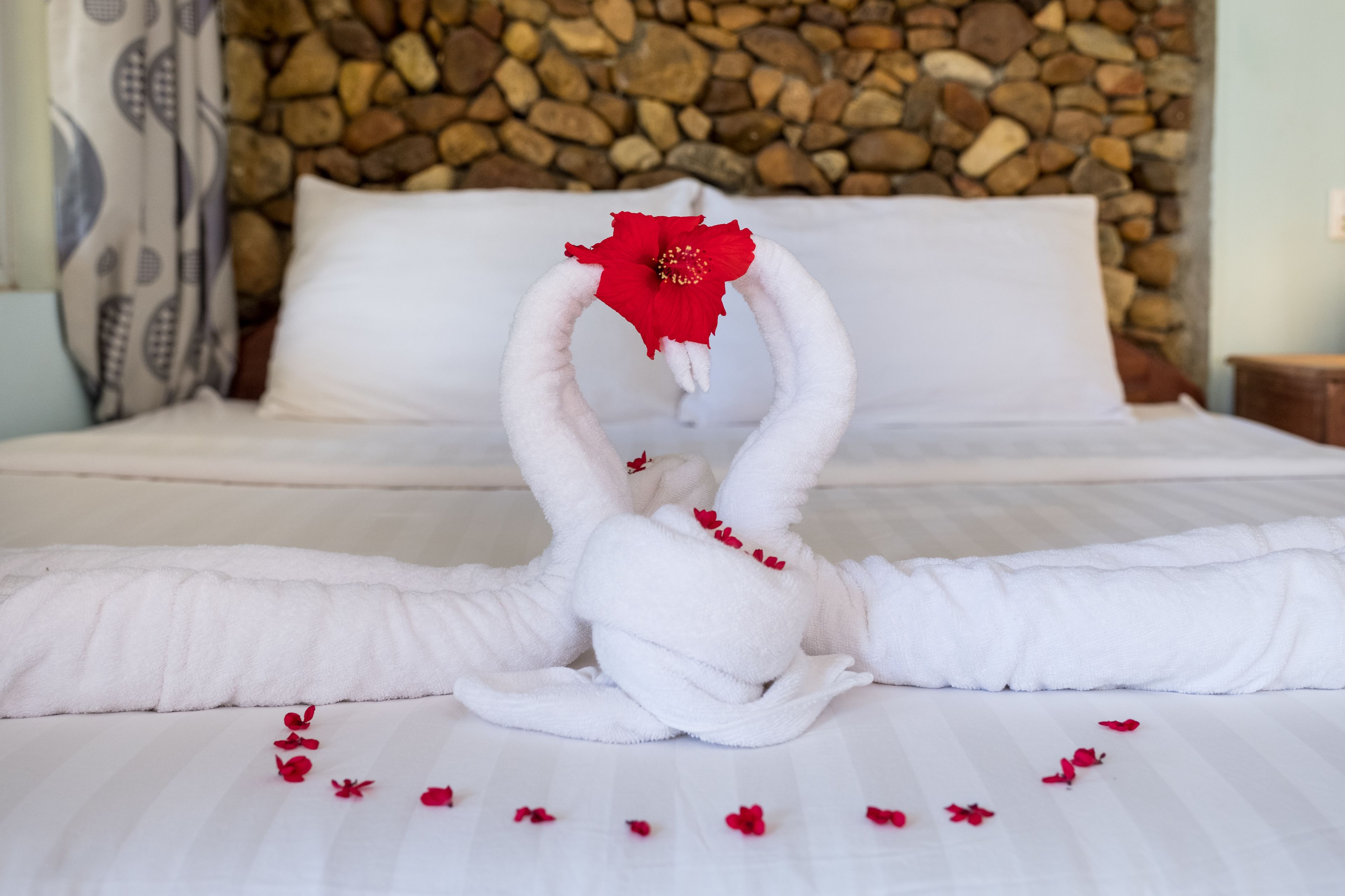 Ein Bett mit weißer Decke und Kissen, dahinter eine Steinsäule und ein rotes Blumendekor.