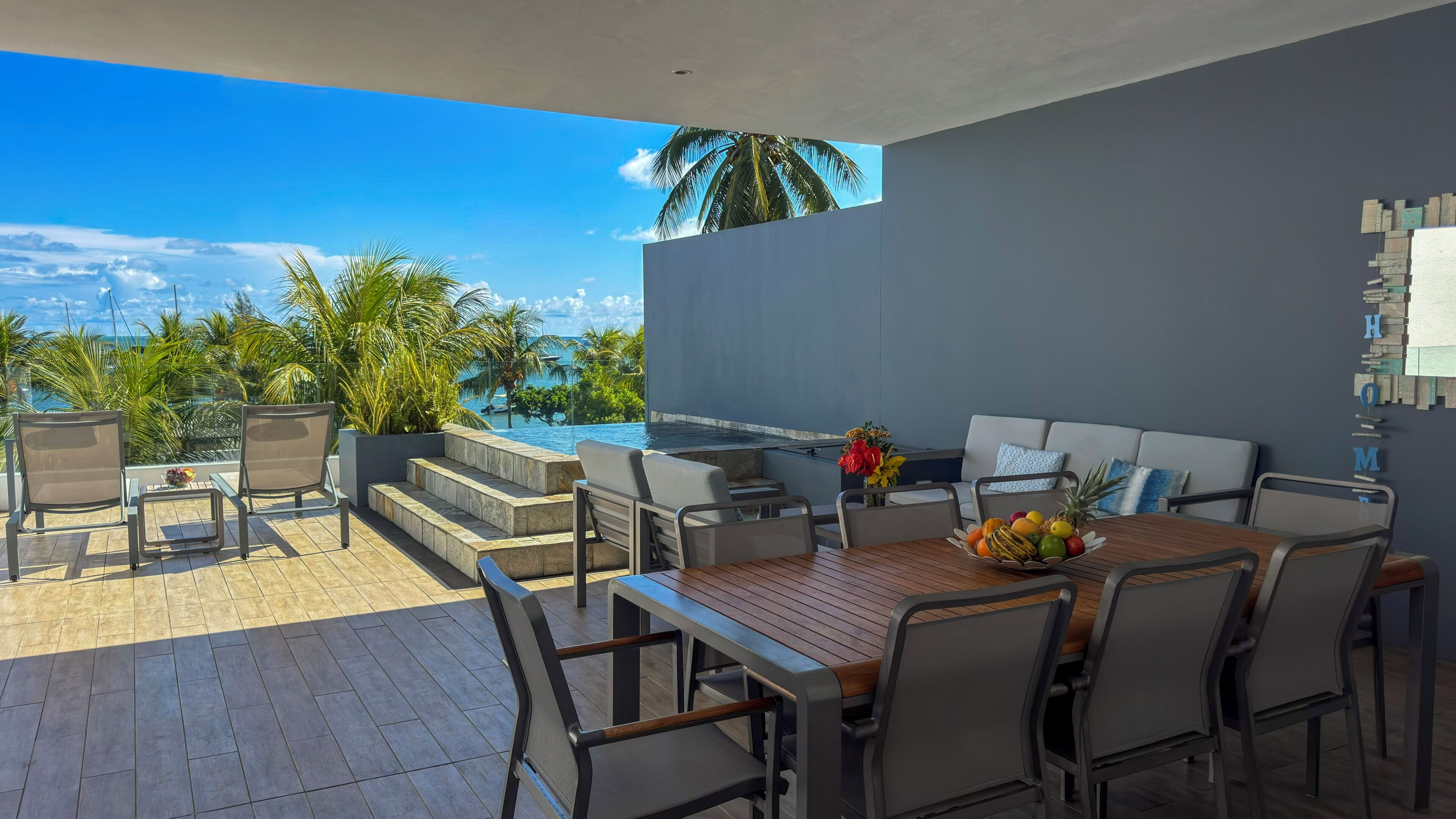 A patio with a wooden table, chairs, and a view of the ocean.