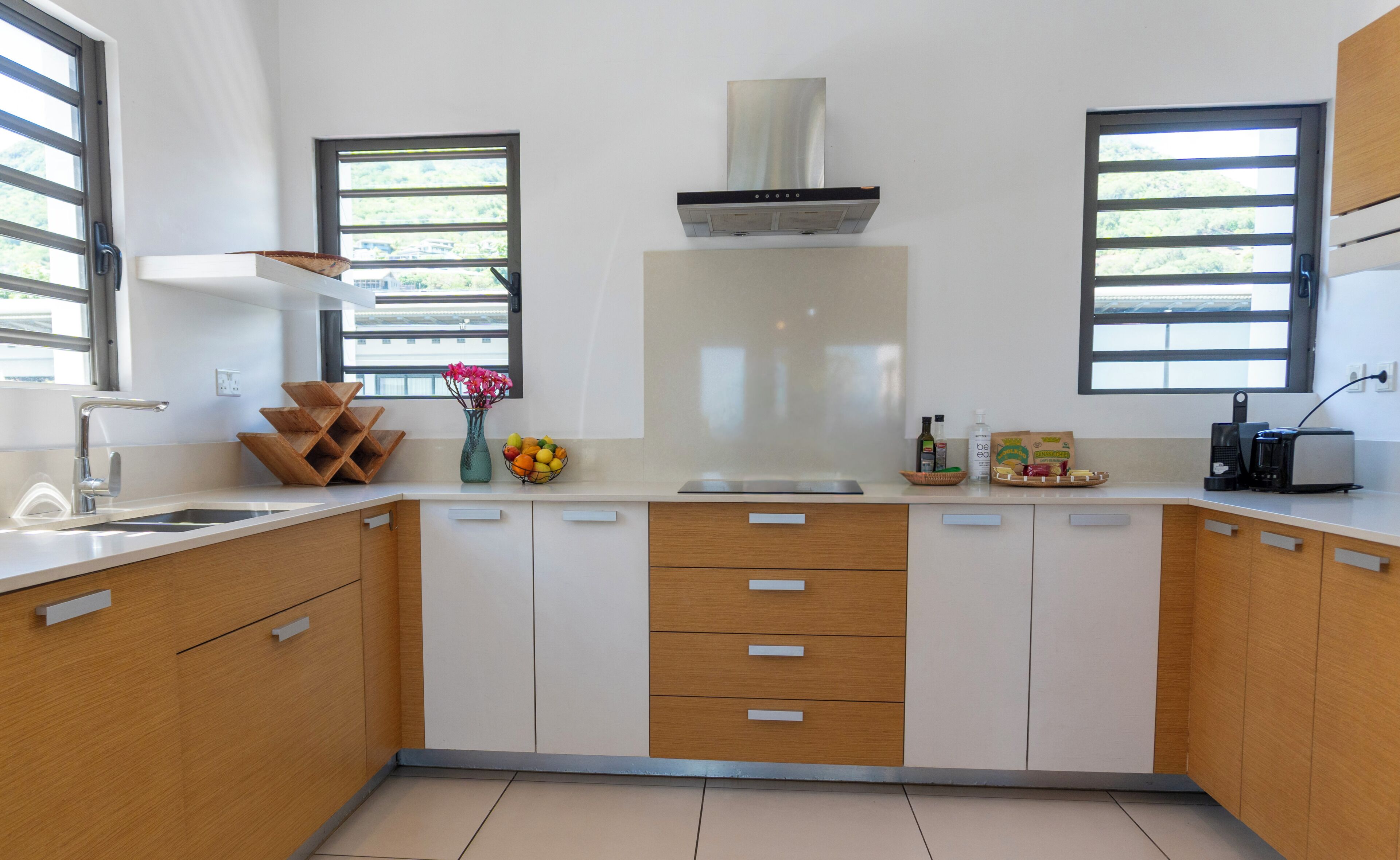 A modern kitchen with a stainless steel range hood, wooden cabinets, a built-in sink, and a window with blinds.