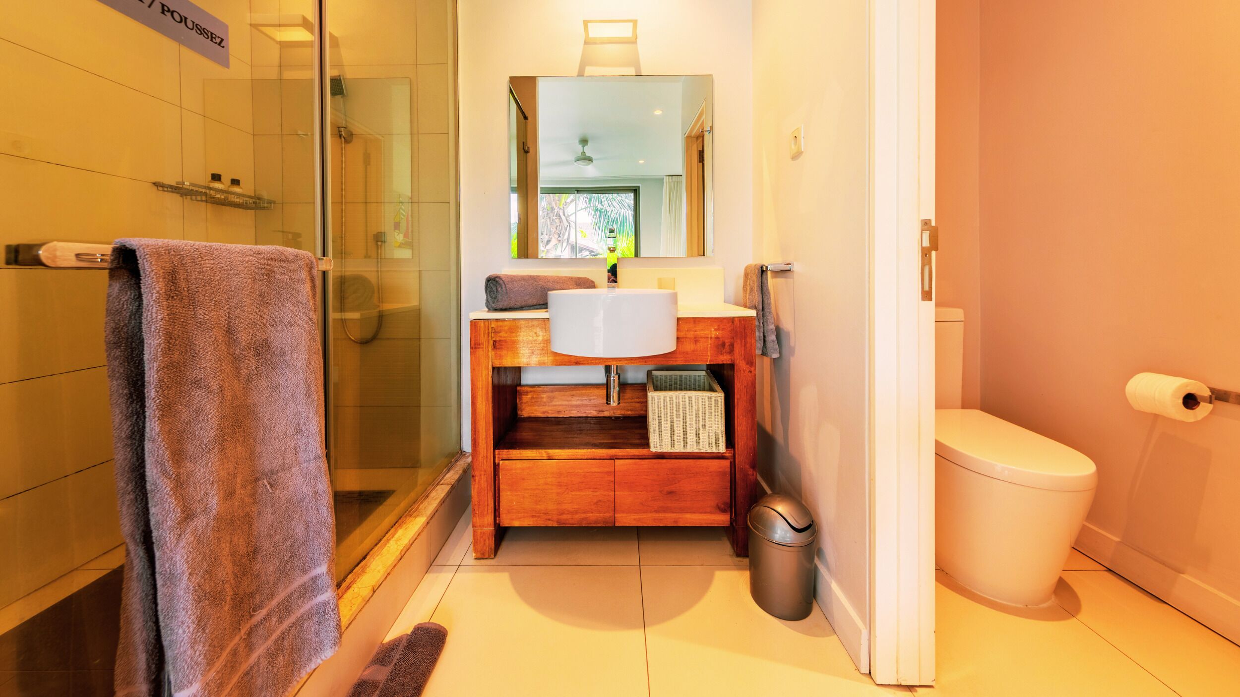 A bathroom with a glass shower enclosure, a wooden vanity with a white sink, a mirror above the sink, and a toilet.