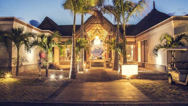 A resort entrance with a thatched roof, palm trees, and a golf cart.