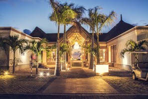 A resort entrance with a thatched roof, palm trees, and a golf cart.