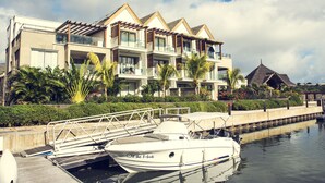 A modern hotel with a poolside area, a boat dock, and a thatched-roof structure.