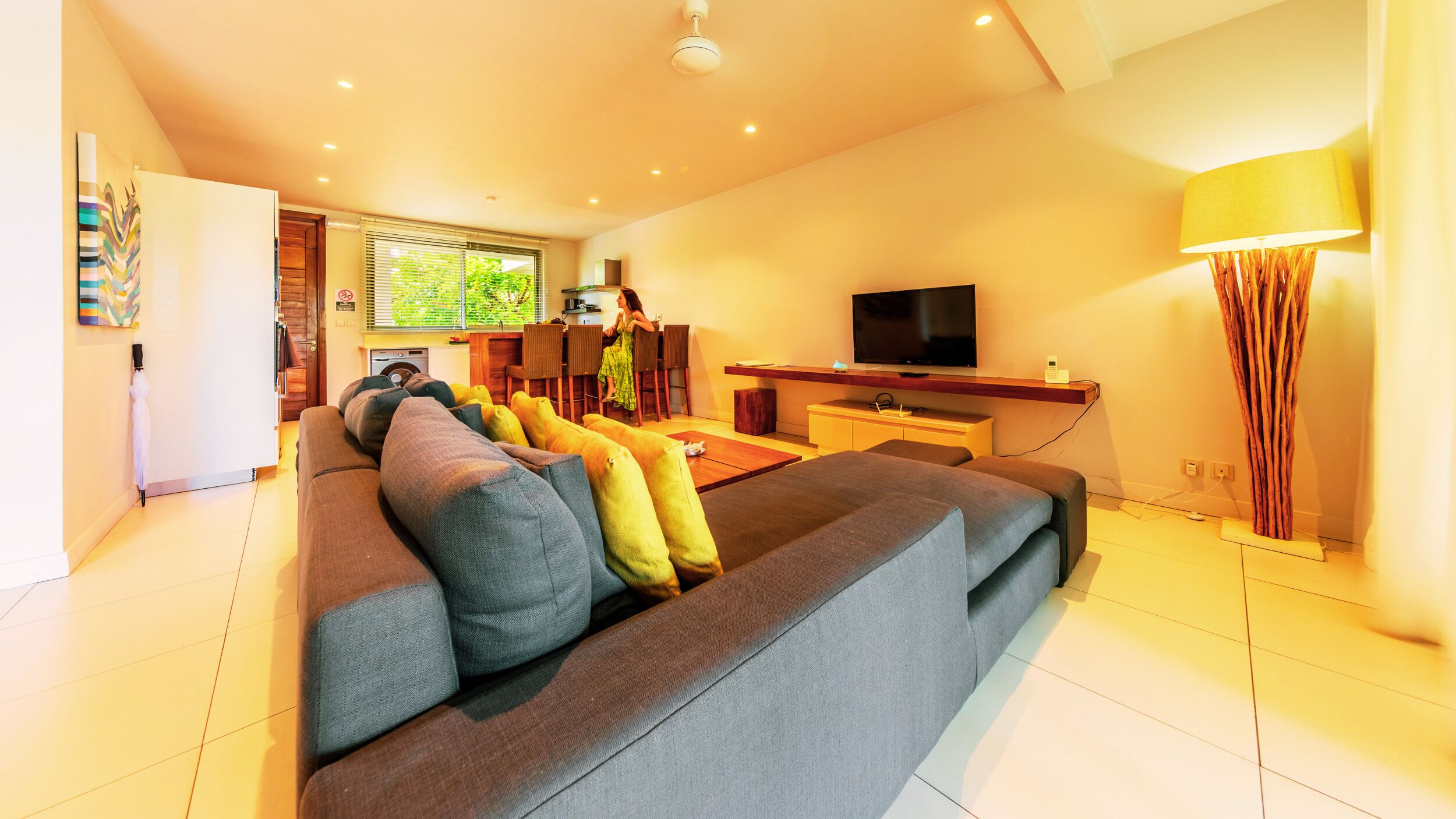 Una sala de estar moderna con un sofá grande de color gris, un televisor de pantalla plana y un comedor con muebles de madera.