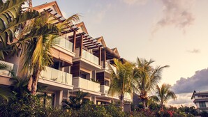 A modern multi-story building with balconies, surrounded by lush tropical vegetation.