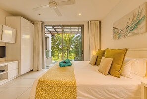 Hotelkamer met een bed, een televisie, een plafondventilator en uitzicht op palmbomen door het raam.