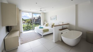 A modern bedroom with a large bed, a freestanding bathtub, and a sliding glass door leading to a balcony.
