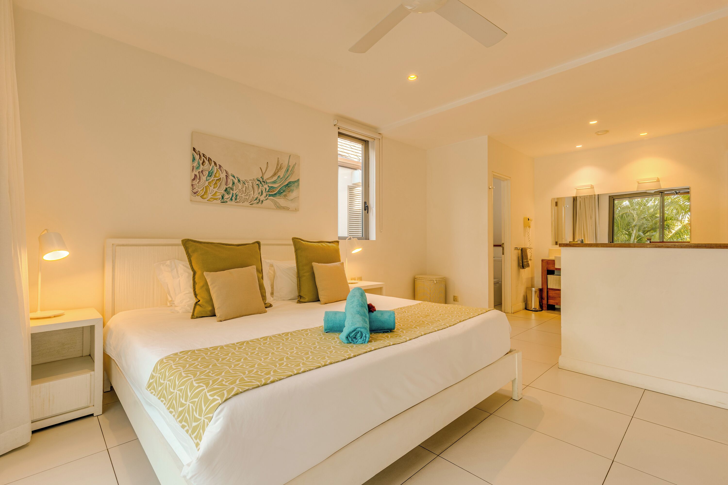A spacious bedroom with a large bed, a bedside table, a nightstand, a window with blinds, and a view of the outdoors.