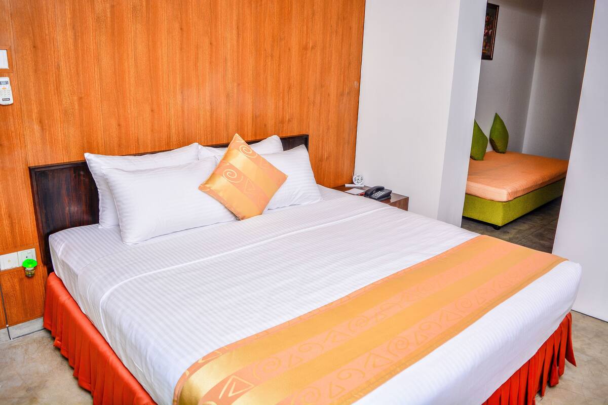 A neatly made bed with a white and orange bedspread, a wooden headboard, and a nightstand with a phone and a green object.