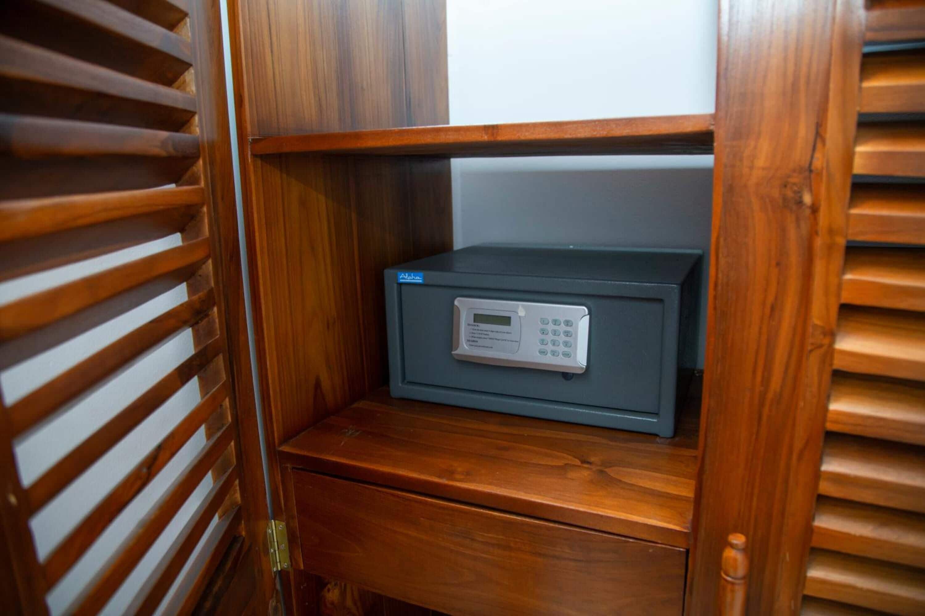 A small, dark-colored safe with a digital keypad, placed on a wooden shelf in a wooden cabinet.