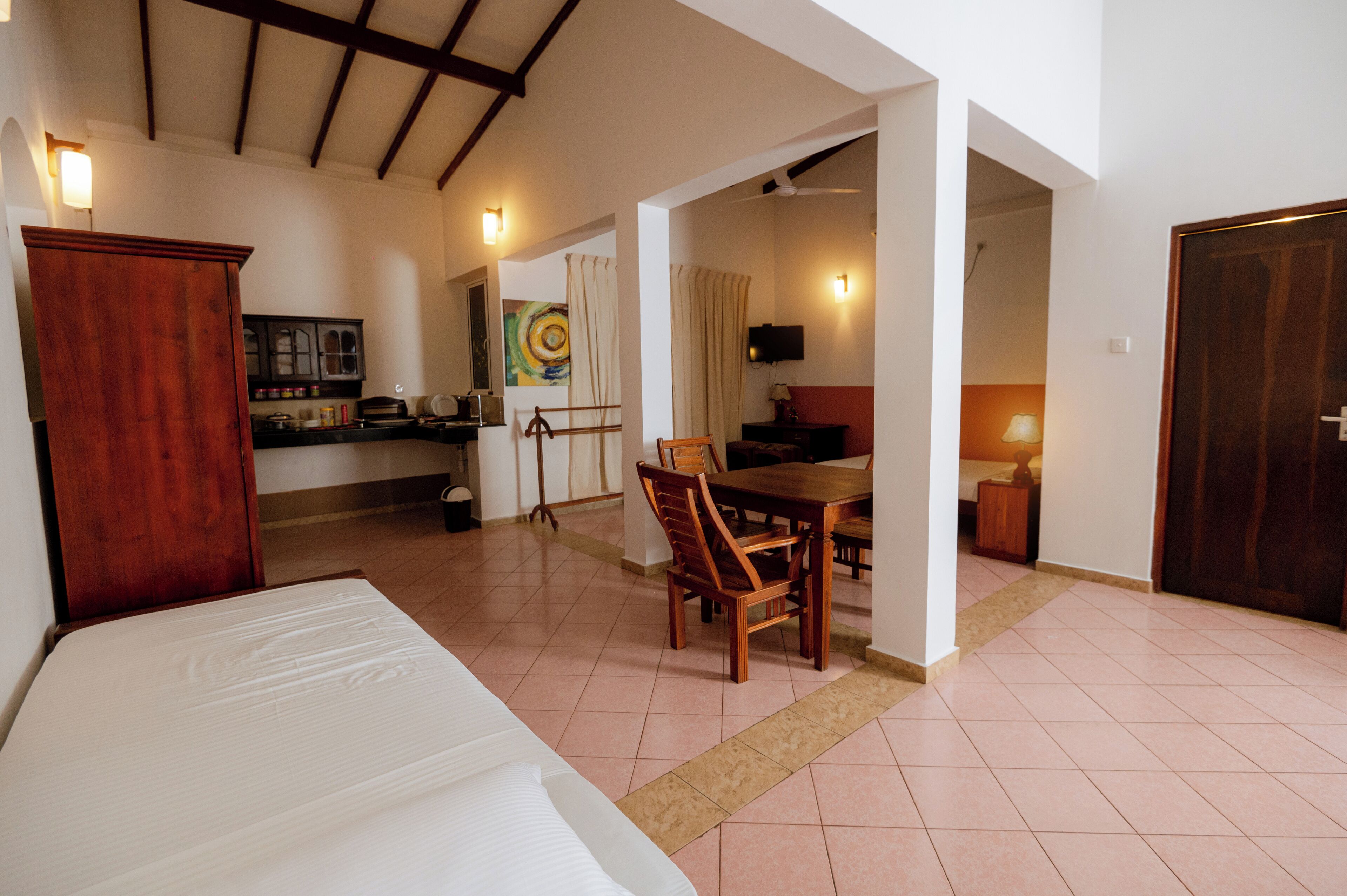 Una habitación con cama, una mesa de comedor con sillas, una zona de cocina y una puerta que da a otra habitación.