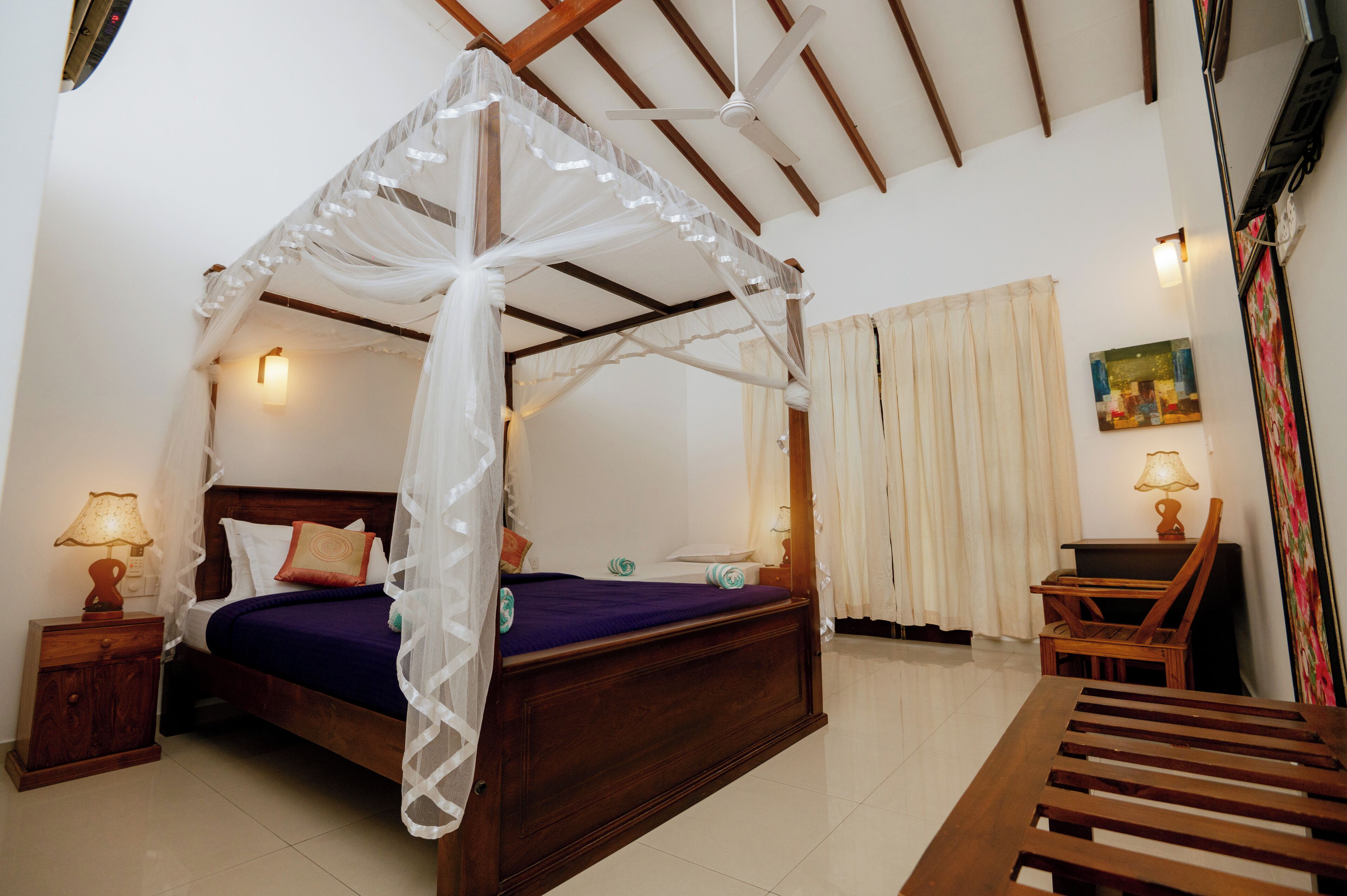 A bedroom with a four-poster bed, a wooden nightstand, a chair, and a desk with a lamp.