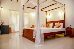 Una cama con dosel y cuatro columnas, ropa de cama blanca, almohadas naranjas, cabecera de madera y una mesita de noche con una lámpara.