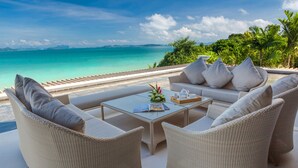 Un espacio al aire libre con luz solar, muebles de mimbre, una mesa de vidrio y vistas al océano.