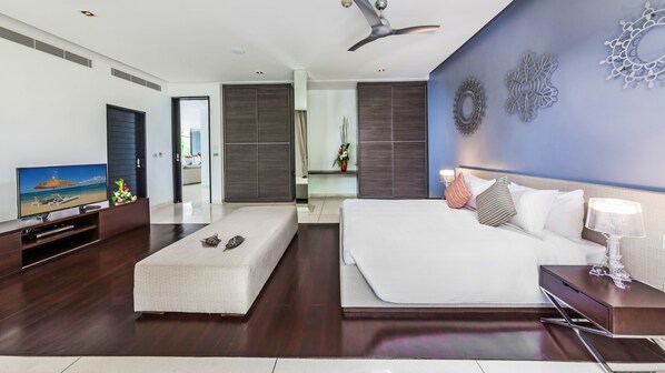 A modern hotel room with a large bed, a TV, and a desk with a lamp.