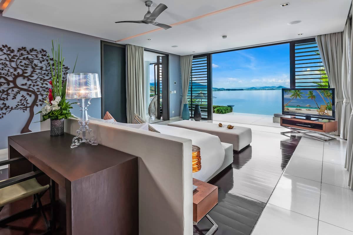 A modern hotel room with a large window, a ceiling fan, a flat-screen TV, a desk with a chair, and a sofa.