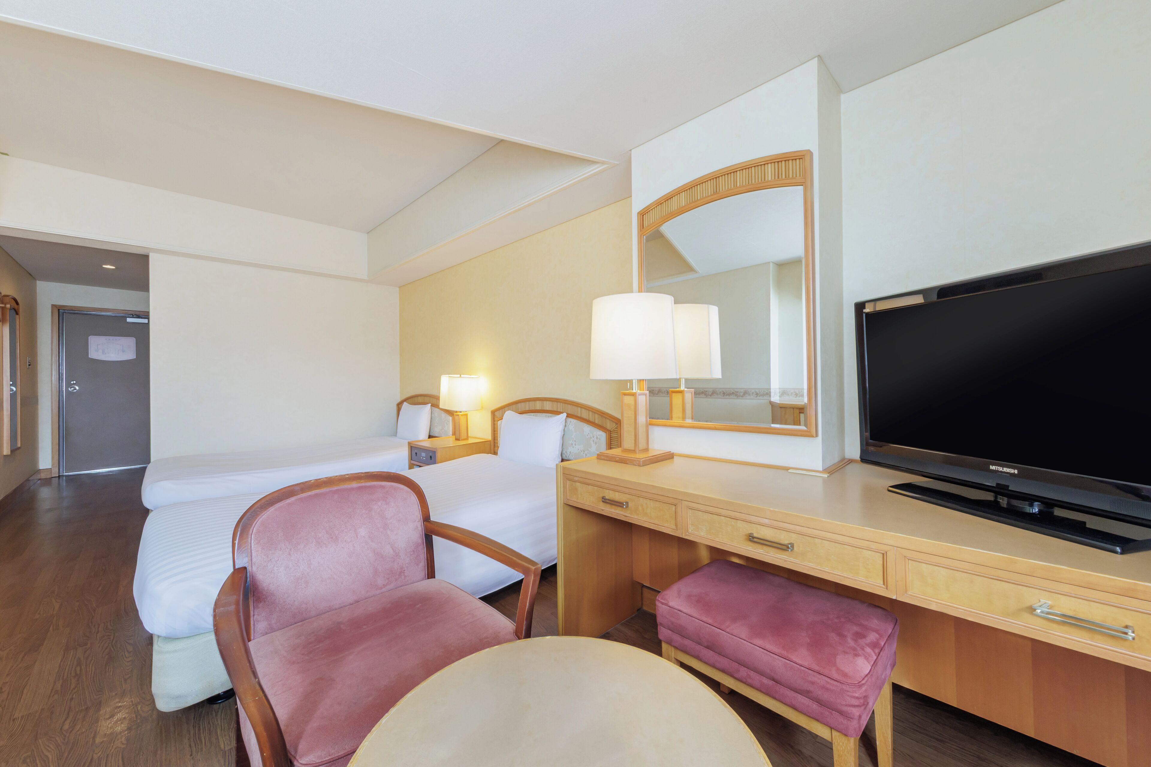 A hotel room with a bed, a desk with a television, a chair, a lamp, and a mirror.