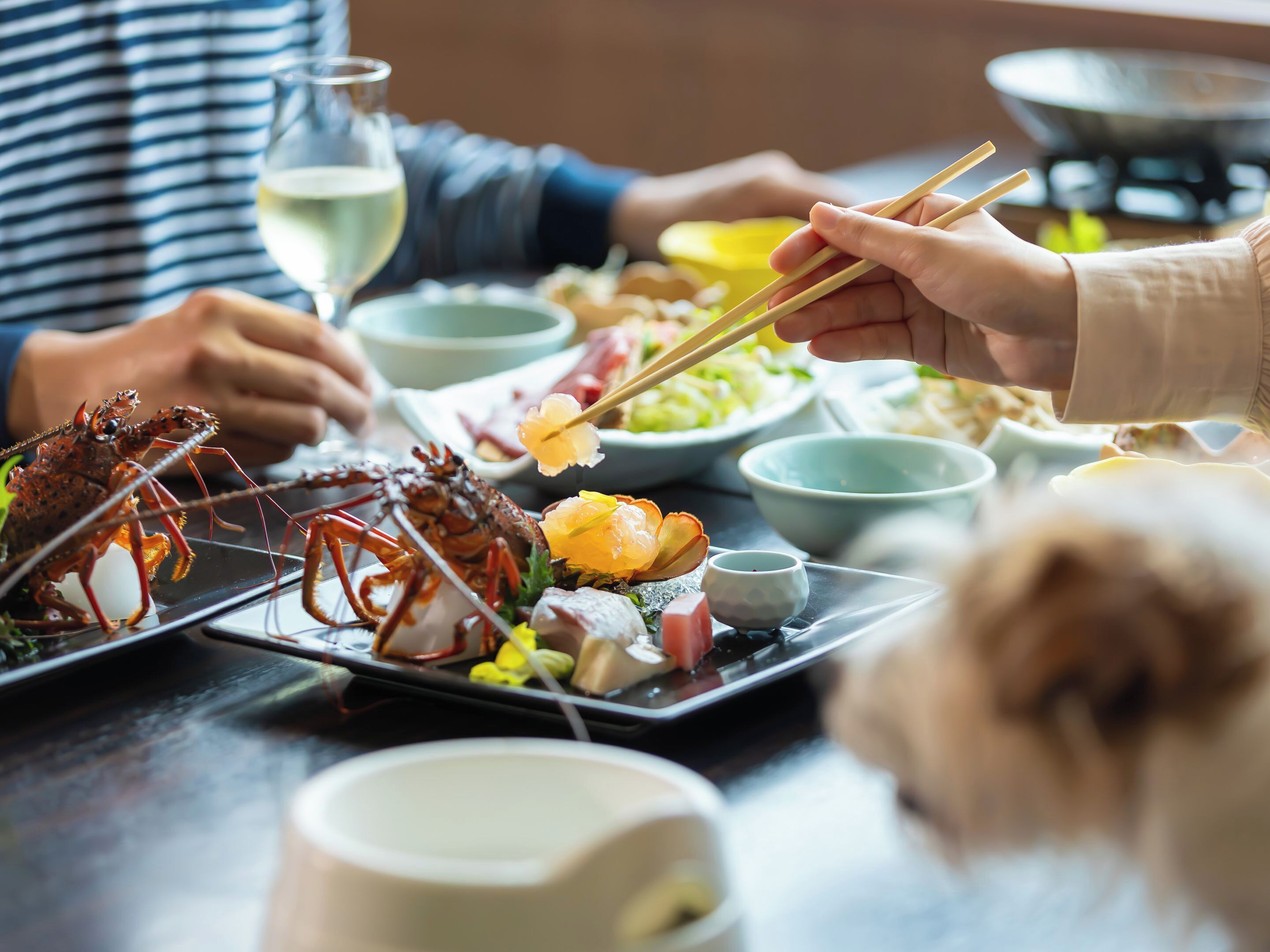 A dining table with various dishes, including seafood and vegetables, and a glass of white wine.