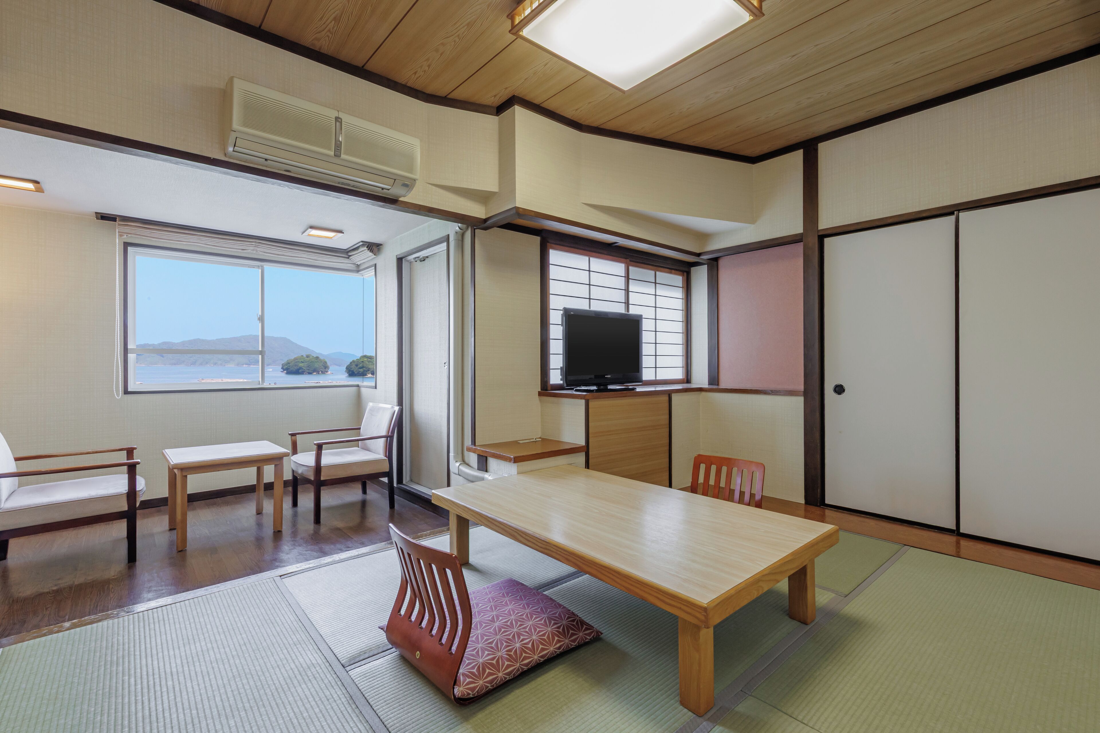 A traditional Japanese room with tatami flooring, a low table, chairs, a television, and sliding doors.