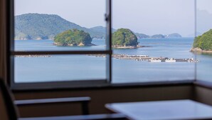A room with a large window overlooking a calm bay with several islands and a dock. - Wan Wan Paradise Toba (Toba)