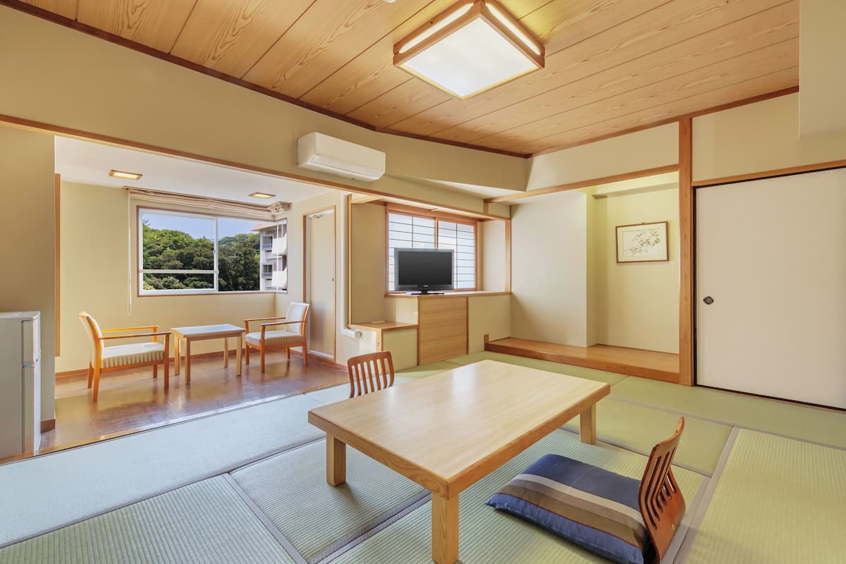 A traditional Japanese room with tatami flooring, a wooden table, chairs, a television, and a sliding door.