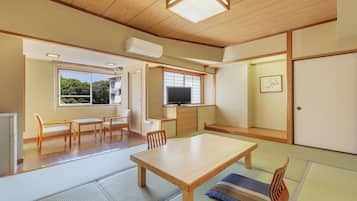 Una habitación japonesa tradicional con suelo de tatami, una mesa de madera, sillas, un televisor y una puerta corredera.