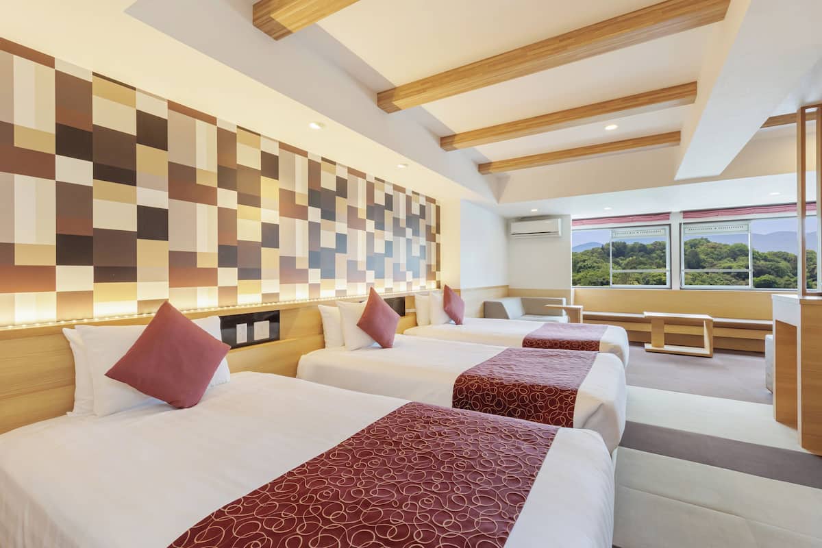 A hotel room with three beds, a large window with a view, and a modern wall design.