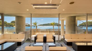 A modern lounge area with a view of the sea and hills, featuring comfortable seating and a glass partition.