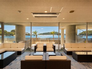 Un moderno espacio de descanso con vistas al mar y colinas, que ofrece asientos cómodos y un divisor de vidrio.