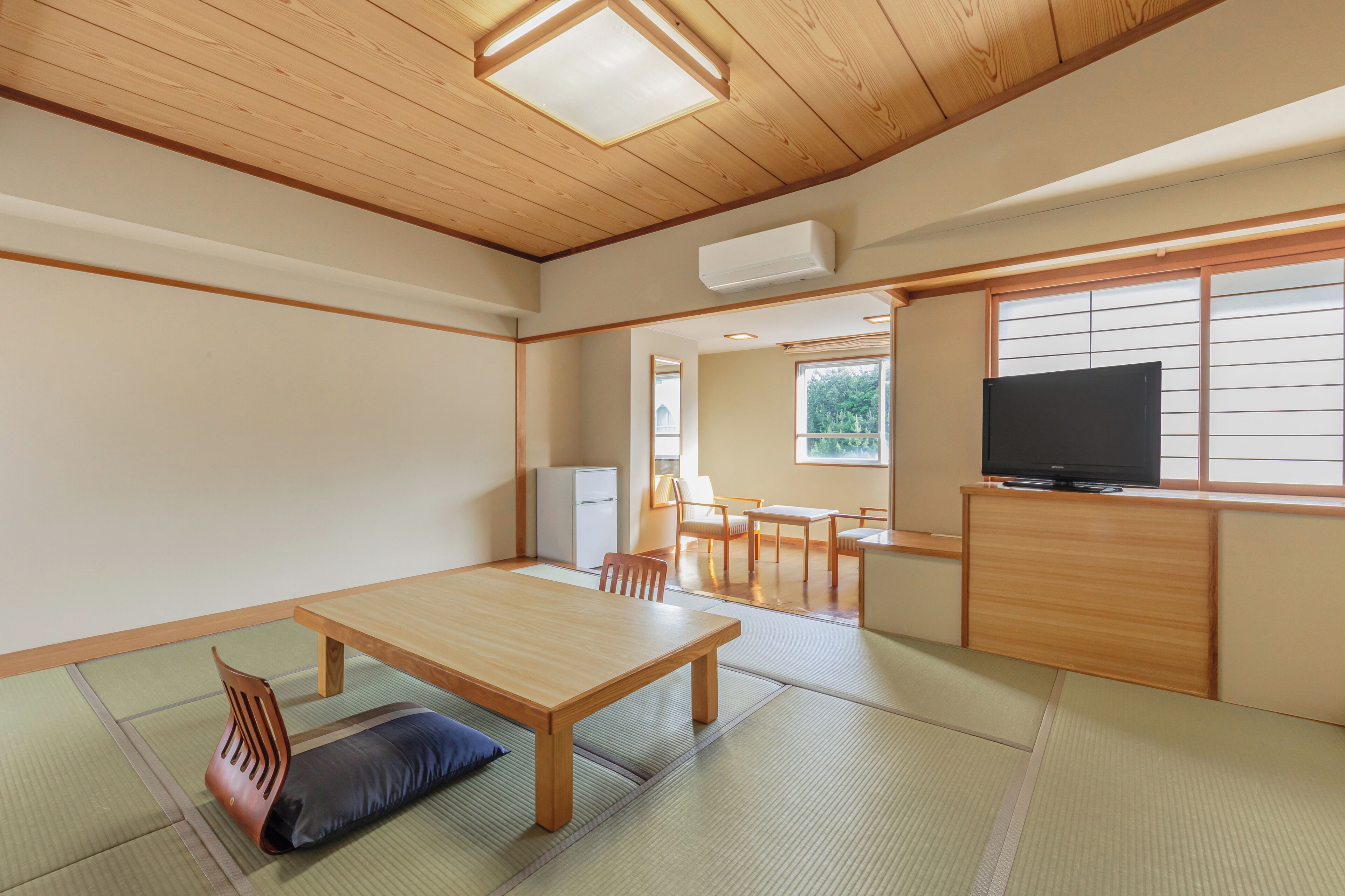 A traditional Japanese room with tatami flooring, a low wooden table, a television on a wooden stand, and a sliding door leading to another room.