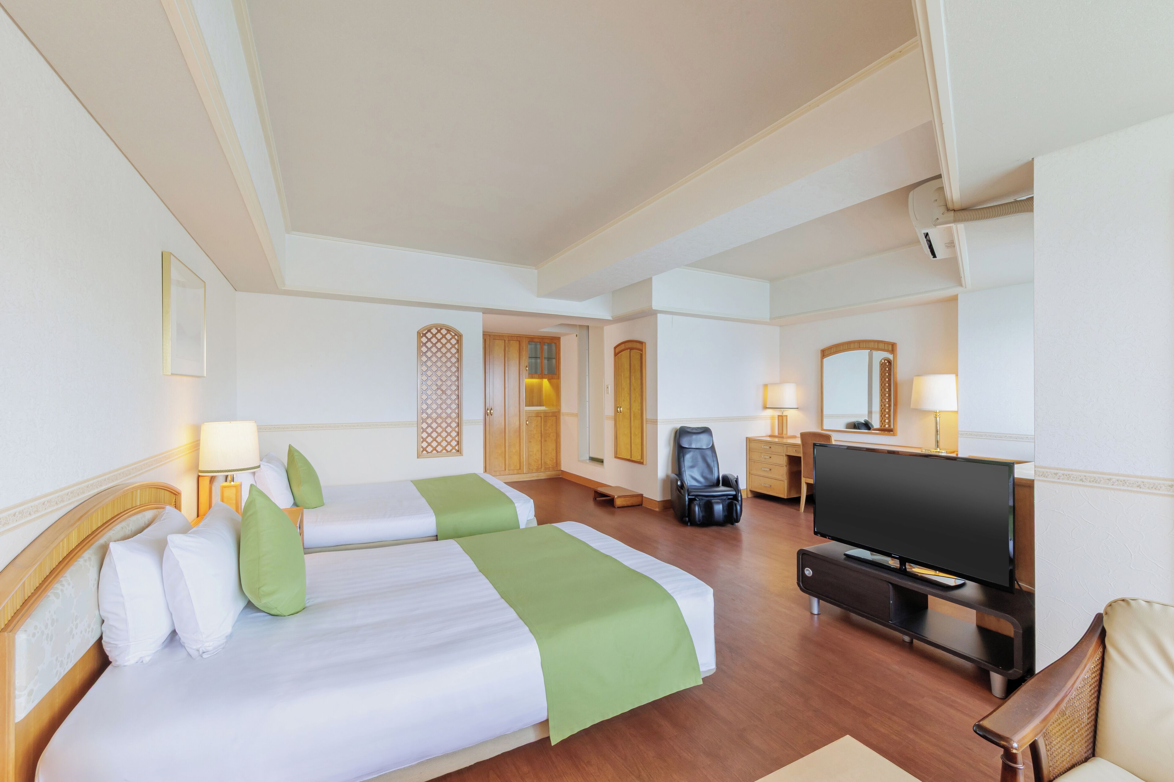 Ein Hotelzimmer mit zwei Betten, einem Fernseher, einem Schreibtisch und einem Sessel.