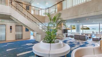 A spacious lobby with a central seating area, a staircase, and a view of the sea.