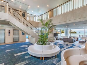 Un vestíbulo amplio con un área de estar central, una escalera y vista al mar.