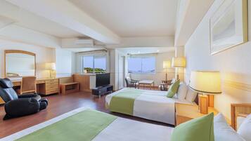 A hotel room with two beds, a desk, a chair, a TV, and a view of the sea.